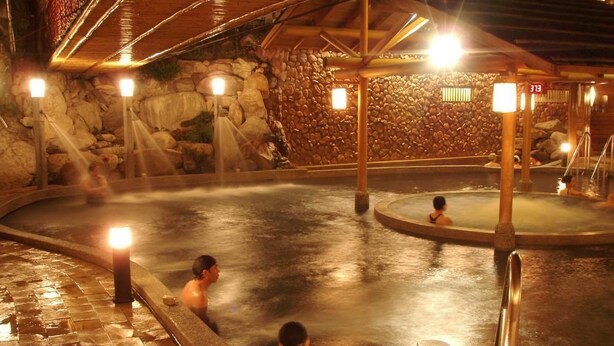A hot spring area with stone walls and wooden beams, featuring multiple hot tubs and illuminated by warm lighting. - Ku Kuan Hotspring Hotel (Taichung)