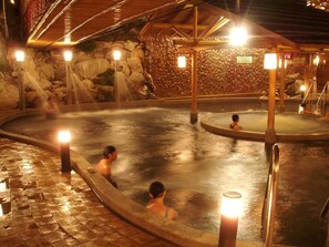 A hot spring area with stone walls and wooden beams, featuring multiple hot tubs and illuminated by warm lighting. - Ku Kuan Hotspring Hotel (Taichung)