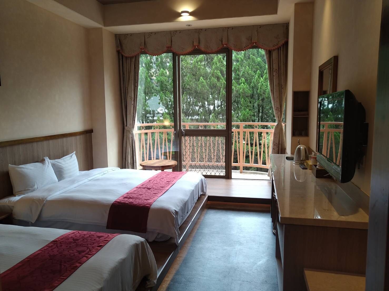 A hotel room with two beds, a balcony with a wooden railing, a television, and a small table.