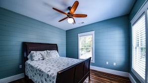 A bedroom with a bed, a ceiling fan, a window, and wooden flooring.