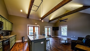 A spacious living area with a kitchen, wooden floors, and a ceiling fan.