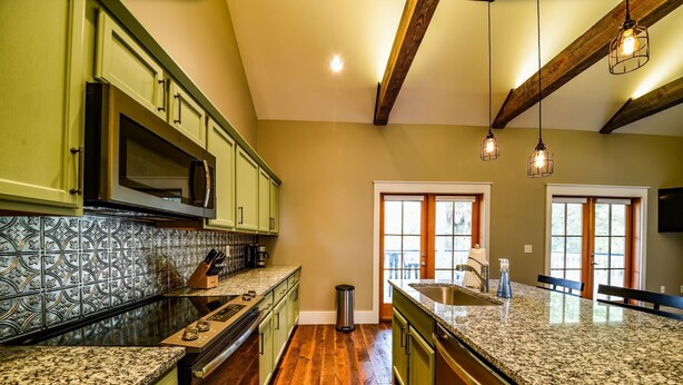 A kitchen with green cabinets, a granite countertop, and a wooden ceiling.