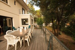 A deck with a table and chairs, surrounded by trees and a building with a balcony.