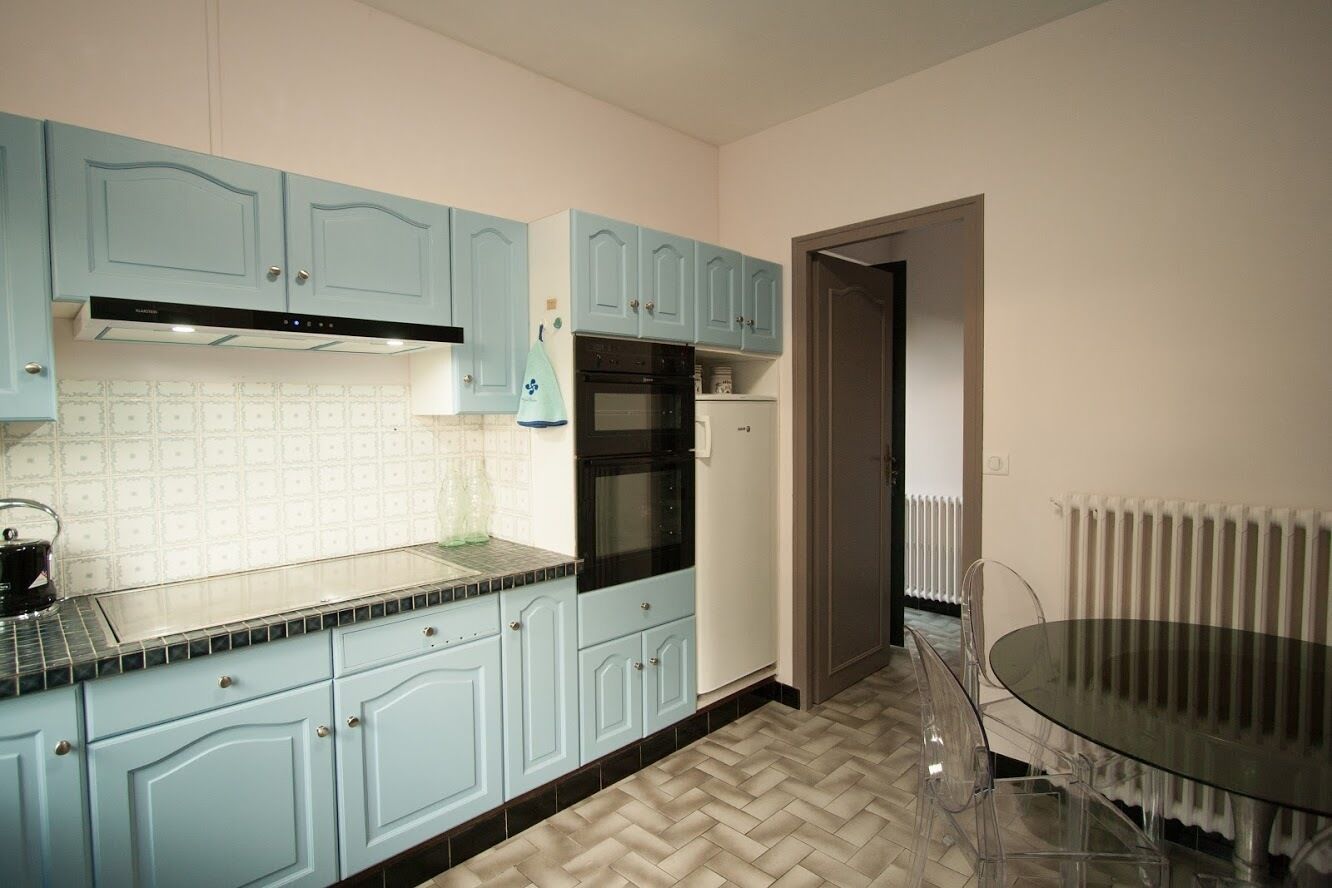 Een keuken met lichtblauwe kastjes, een zwarte oven en een glazen tafel.