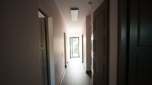 Un corridoio stretto con un lampadario a soffitto e una porta in fondo che dà su un ambiente luminoso.