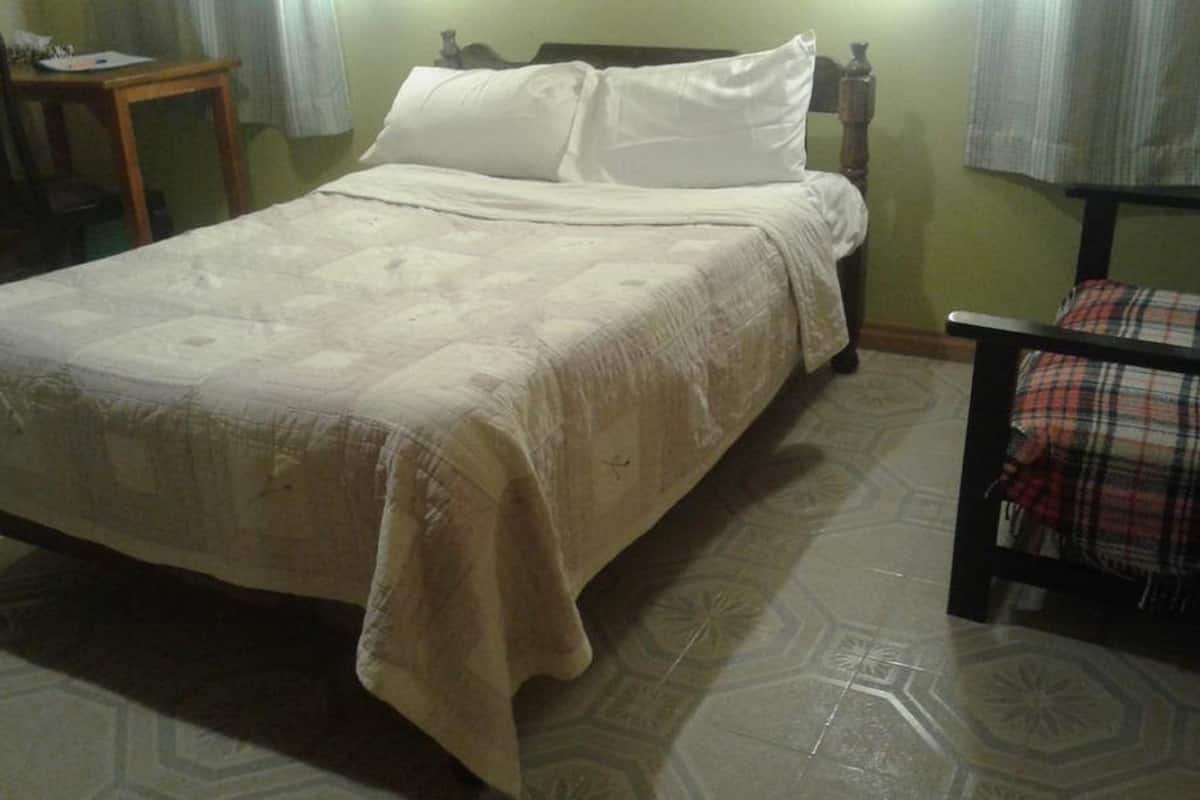 Un lit recouvert d’une couvre-lit beige et orné d’oreillers blancs, dans une pièce dont le sol est recouvert de carreaux décoratifs.