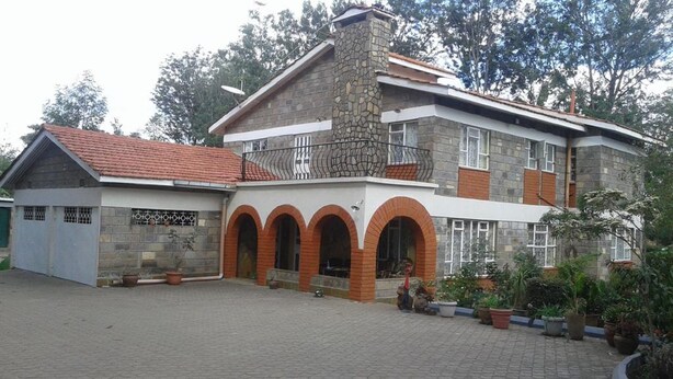 Una casa de dos pisos con fachada de piedra, techo de tejas rojas y patio empedrado.