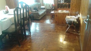 Un salón con suelo de madera, un sofá, sillas, una mesa de centro y una mesa de comedor con sillas.