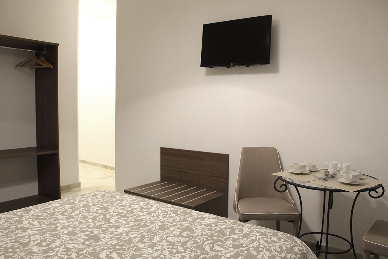 Ein Hotelzimmer mit einem Bett, einem Sessel, einem Tisch mit Tassen und einem an der Wand befestigten Fernseher.