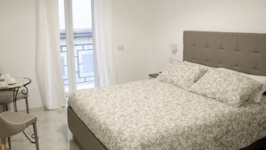 Un dormitorio con cama, mesita de noche, una silla y una ventana con cortinas.