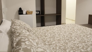 Un dormitorio con una cama, un armario y una mesita con una radio y una caja.