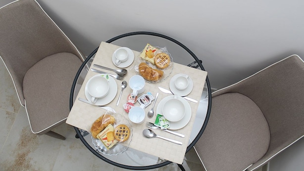 Mesa redonda dispuesta para una comida, con mantel blanco, platos, vasos, cubiertos y refrigerios envasados.