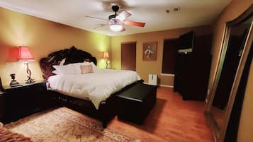 Une chambre à coucher comprenant un lit, des lampes de chevet, un ventilateur de plafond, une table de chevet, une commode et une porte donnant sur une autre pièce.