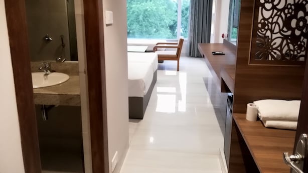 A modern hotel room with a bathroom, a large window, a bed, and a wooden side table. - Lake View Resort (Mawal)