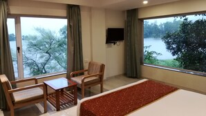 A hotel room with a bed, a table, two chairs, a TV, and a large window with a view of trees and water. - Lake View Resort (Mawal)