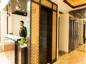 A reception area with a reception desk, a potted plant, and a decorative panel. - Hotel Sangat Regency (Bhopal)