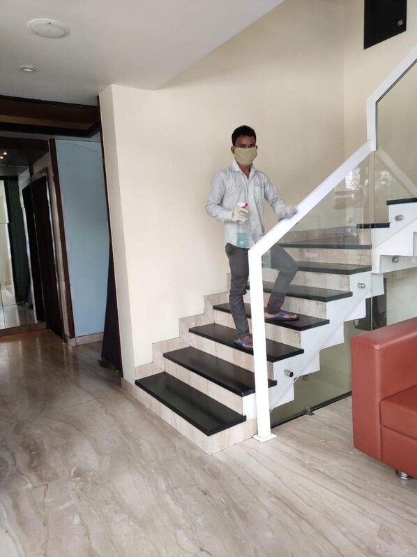 A person descending a modern staircase with glass railings and a handrail, in a room with a light-colored floor and a red accent wall. - Hotel Sangat Regency (Bhopal)