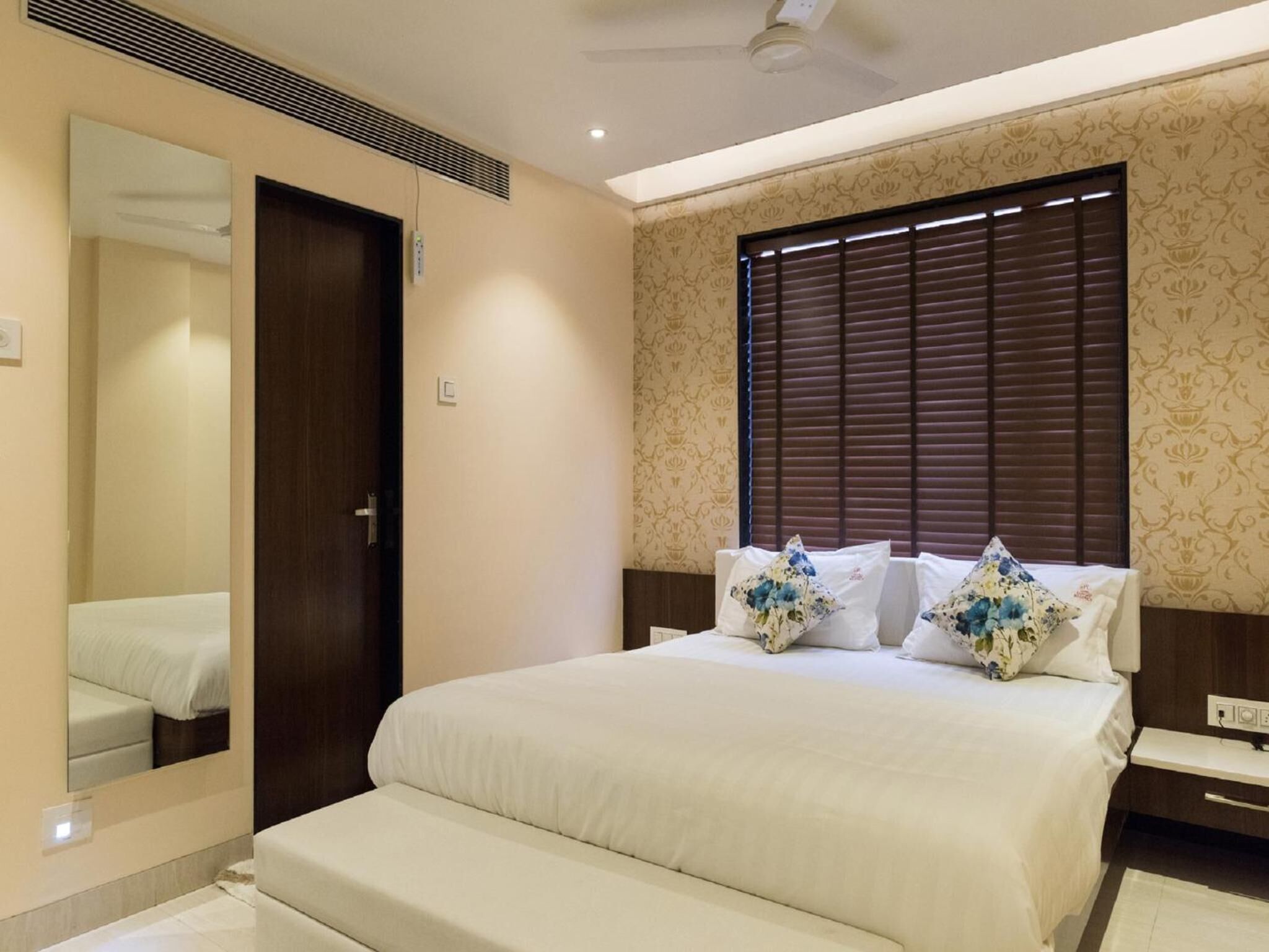 Une chambre d’hôtel avec un grand lit, une table de chevet, un miroir et une fenêtre avec des stores.
