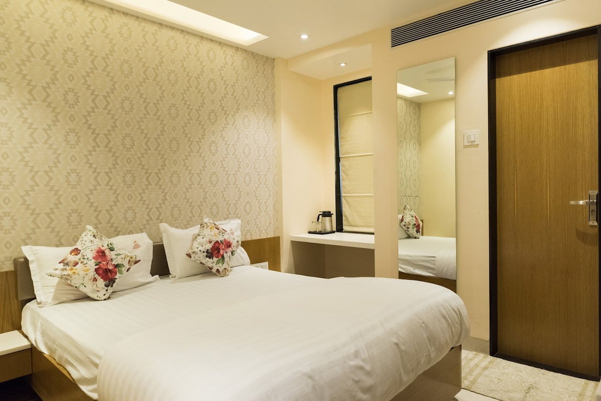 A hotel room with a neatly made bed, a wooden door, and a mirror on the wall.