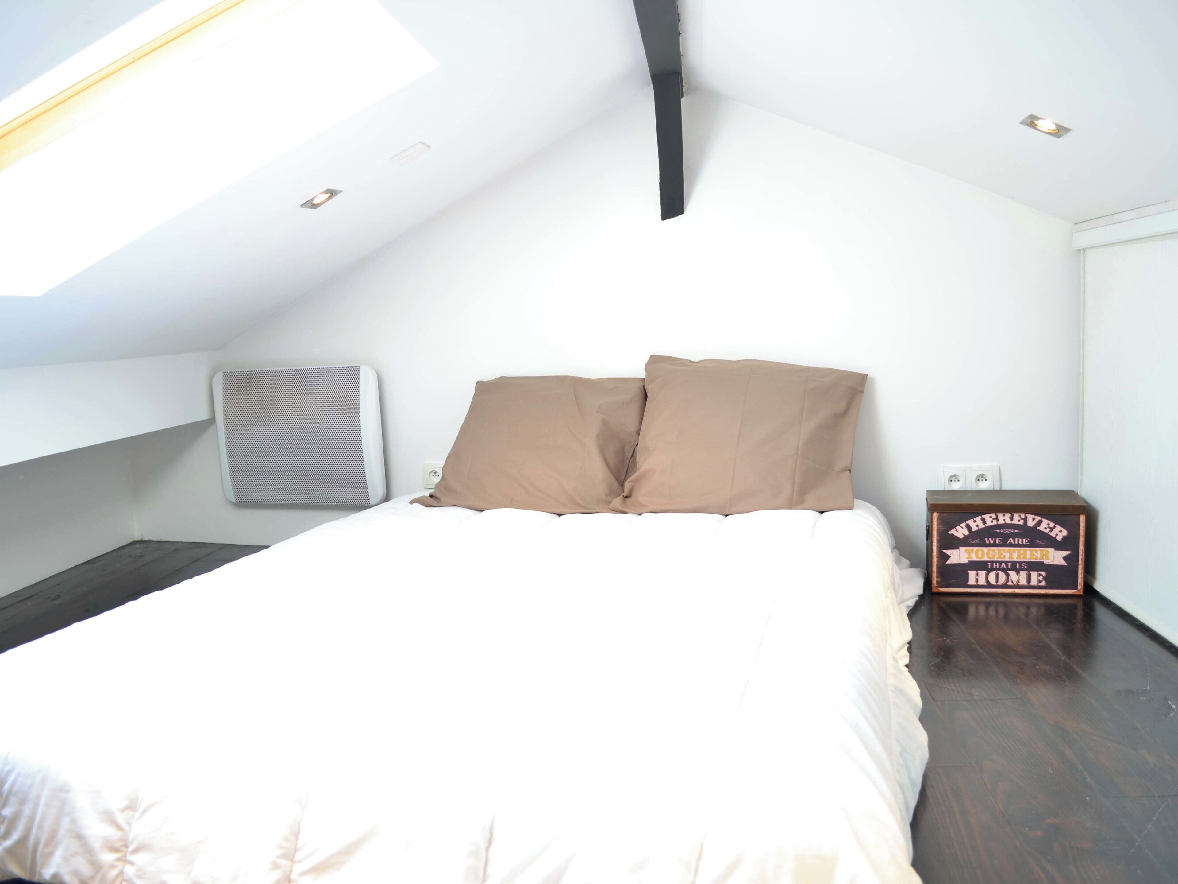 A bedroom with a bed, two pillows, a heater, a wooden box with a message, and a skylight.