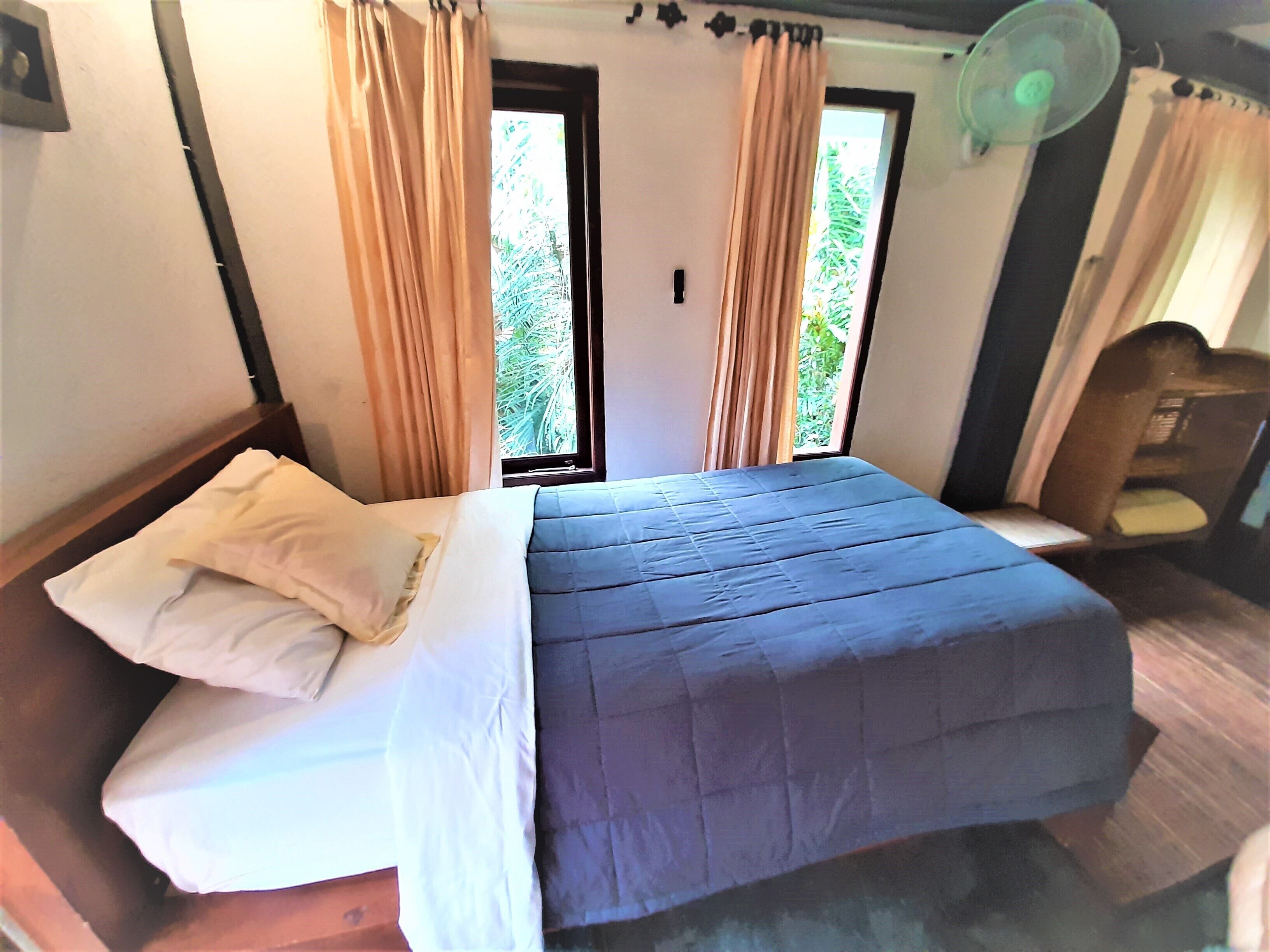 Un lit avec une couverture bleue, une tête de lit en bois et des rideaux beige.