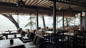 An outdoor seating area with wooden tables and chairs, overlooking a body of water. - Peace Garden Goa (Canacona)