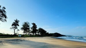 A beach with a clear sky, sandy shore, and trees in the background. - Peace Garden Goa (Canacona)