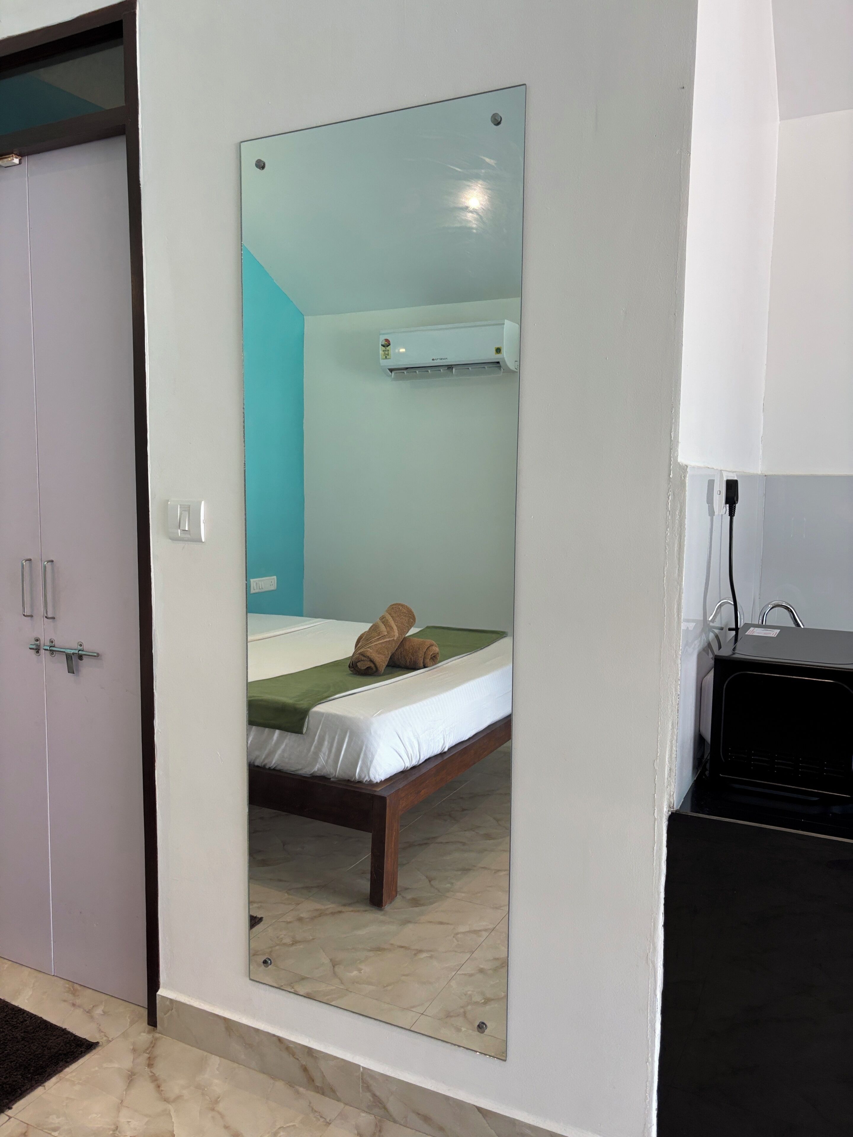 Una habitación con una cama, un espejo, aire acondicionado de pared y una puerta.