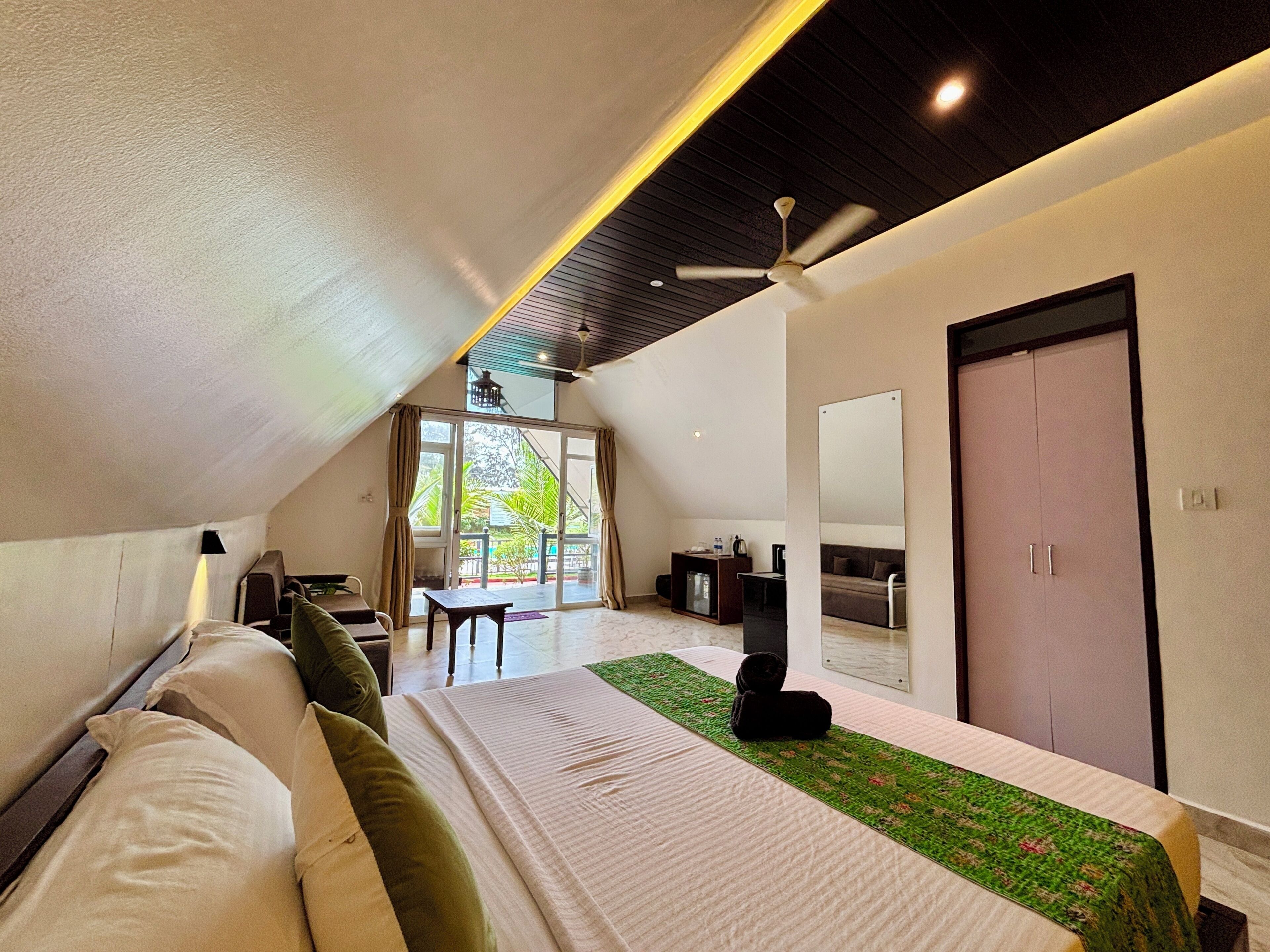 Una habitación de hotel moderna con cama, escritorio, silla, sofá, espejo y ventilador de techo.