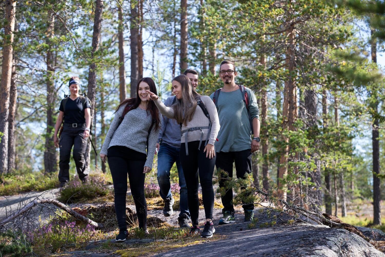 Ryhmä ihmisiä vaeltaa metsäisellä alueella, jossa on puita, ja etualalla näkyy kaatunut puu.