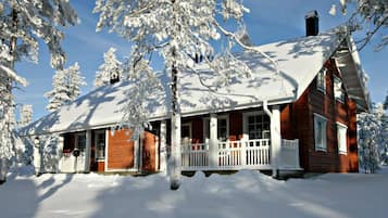 Cozy cabin surrounded by snow-covered trees, featuring a charming porch and a prominent chimney.