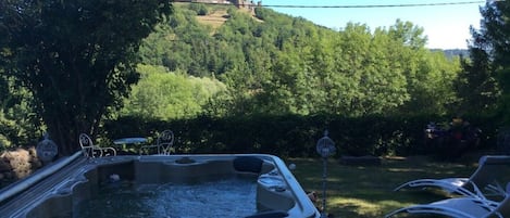 A hot tub with a wooden deck, surrounded by greenery and a view of a castle on a hill.