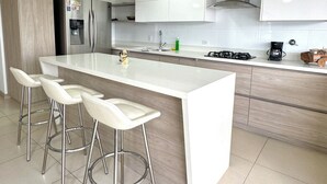 Ett modernt kök med en central köksö, vitvaror i rostfritt stål och vita köksskåp.