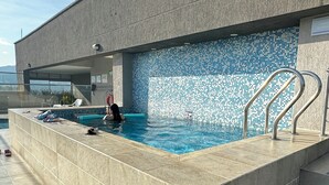 En modern utomhuspool med en vägg dekorerad med ett mosaikmönster, ett metallräcke och en klar himmel.