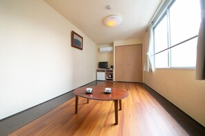 Een kamer met een houten vloer, een ronde tafel met twee kommen, een plafondlamp, een raam en een deur.