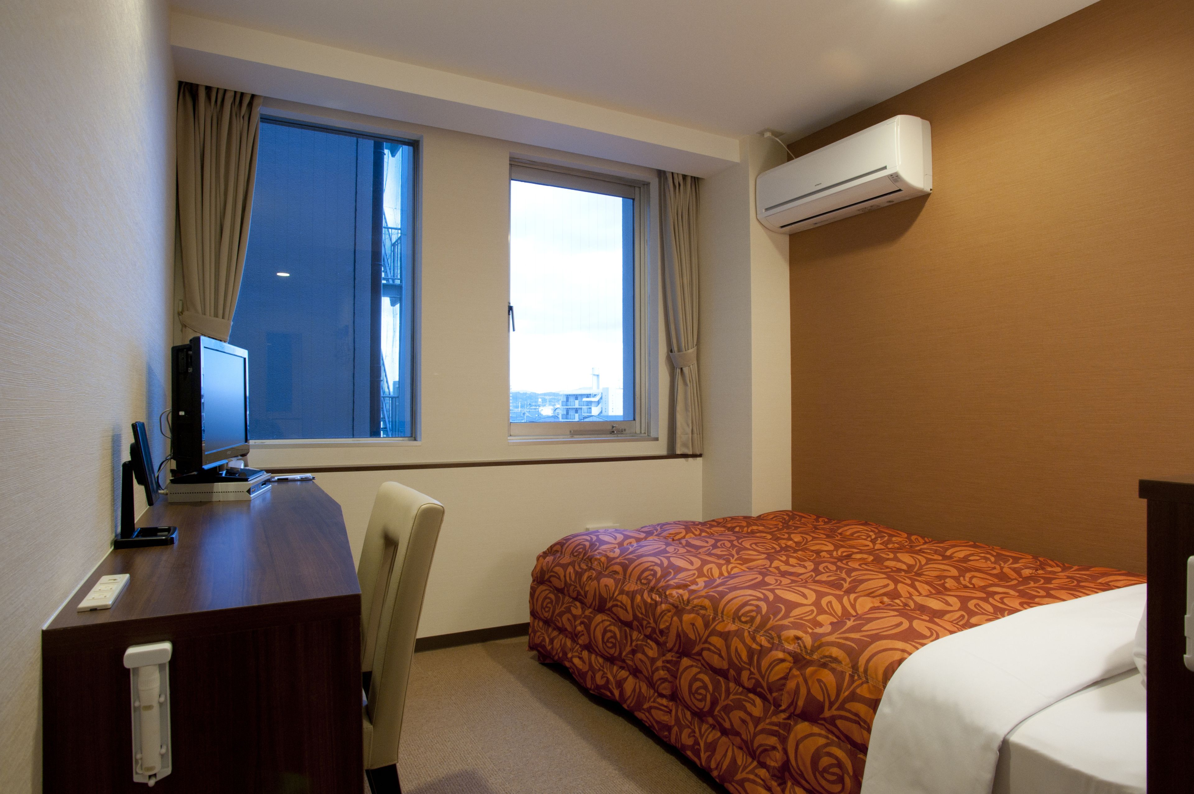 Une chambre d’hôtel équipée d’un bureau, d’un lit avec une couvre-lit à motifs, d’une fenêtre avec des rideaux et d’un appareil de climatisation.