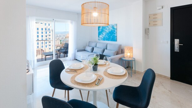 A modern dining area with a round table, blue chairs, and a hanging light fixture. - Lovely apartment, very close to the beach. Wi-Fi A / C With terrace - only families (Playa de Gandía)
