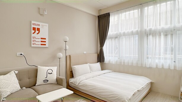 A modern bedroom with a bed, a sofa, a bedside table, and a wall-mounted light fixture. - HoHo Woo Tainan Homestay (Tainan)