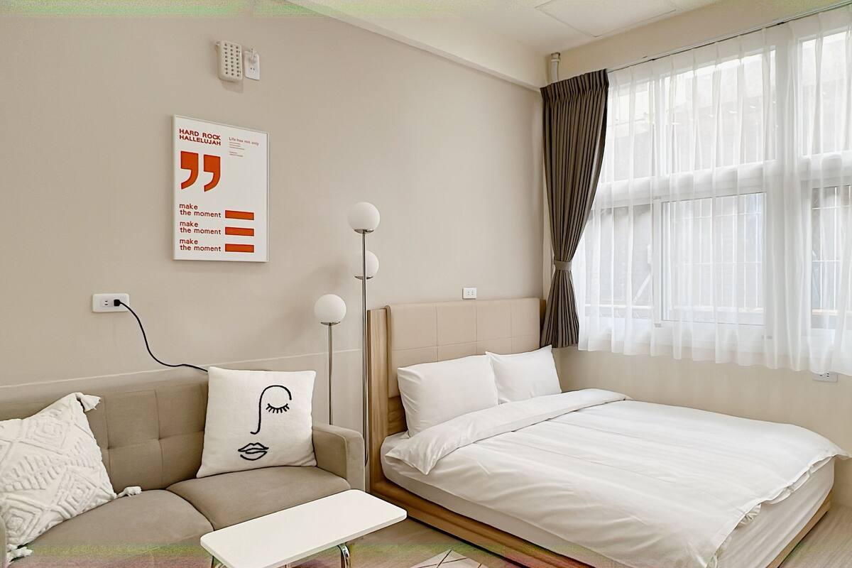 A modern bedroom with a bed, a sofa, a bedside table, and a wall-mounted light fixture.