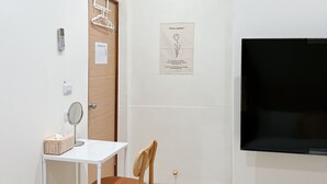 A small, clean room with a white desk, a chair, a mounted TV, and a door with a wooden panel. - HoHo Woo Tainan Homestay (Tainan)