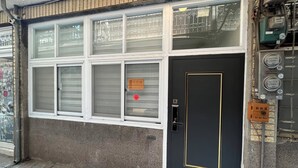 A building facade with a black door, windows with metal grilles, and visible electrical meters. - HoHo Woo Tainan Homestay (Tainan)