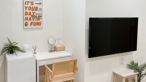 A modern, minimalist room with a white desk, a flat-screen TV, a small refrigerator, and a wicker chair. - HoHo Woo Tainan Homestay (Tainan)