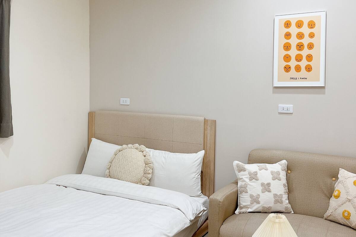 A bedroom with a bed, a sofa, a bedside table, and a wall-mounted picture.