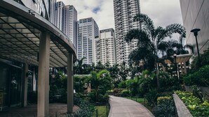 Un edifici modern amb una passarel·la corba, envoltat de vegetació exuberant i alts edificis residencials al fons.