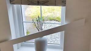 A staircase with a textured carpet, a window with a view of greenery outside, and a white vase on the windowsill. - The Corner Cottage Sandwick (Sandwick)