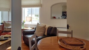 A cozy living room with a leather sofa, a wooden coffee table, and a dining table with a woven placemat. - The Corner Cottage Sandwick (Sandwick)