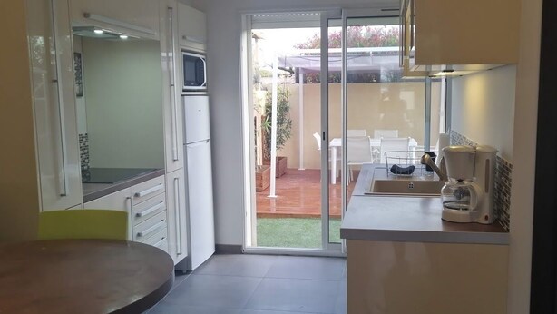 A compact kitchen with white cabinets, a microwave, a coffee maker, and a sliding glass door leading to an outdoor patio. - Gîte 1 bed, sleeps 3, garden and parking, small swimming pool, 15 mins from the sea. (La Crau)