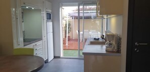 A compact kitchen with white cabinets, a microwave, a coffee maker, and a sliding glass door leading to an outdoor patio. - Gîte 1 bed, sleeps 3, garden and parking, small swimming pool, 15 mins from the sea. (La Crau)