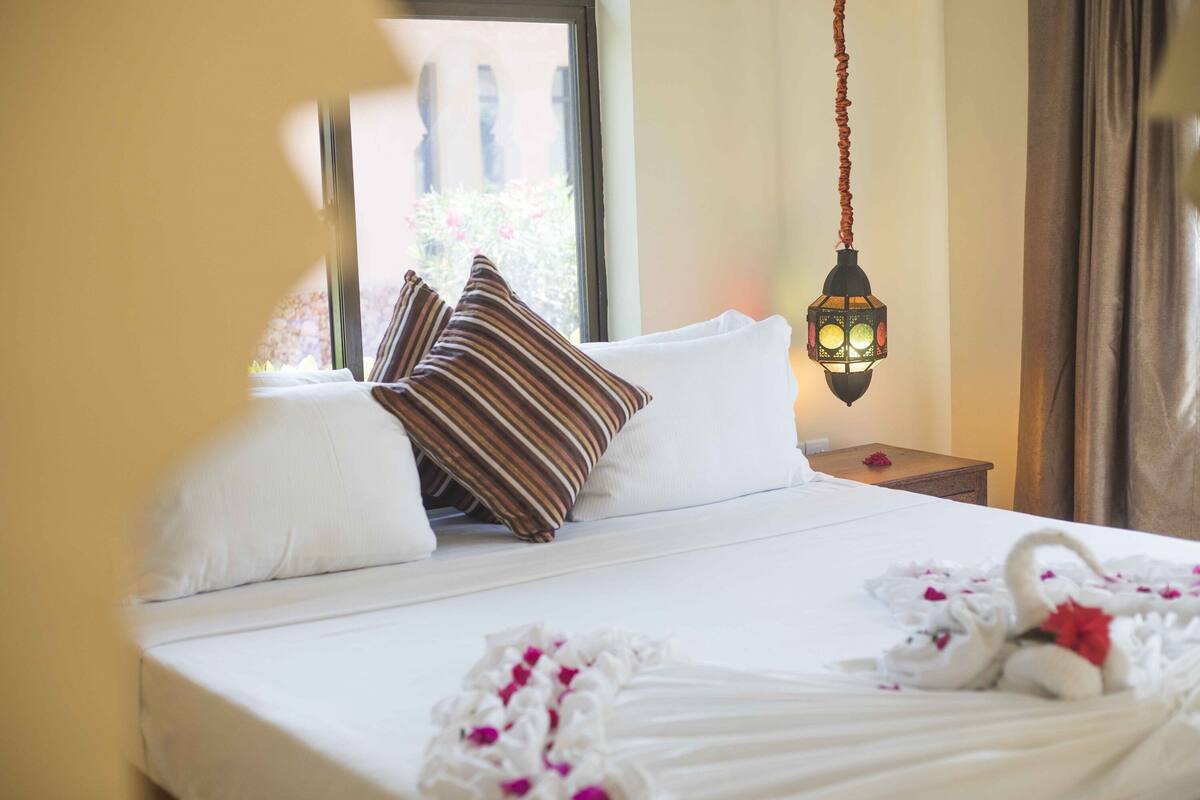 Una cama bien hecha con sábanas blancas, almohadas a rayas y un arreglo decorativo con cisnes.