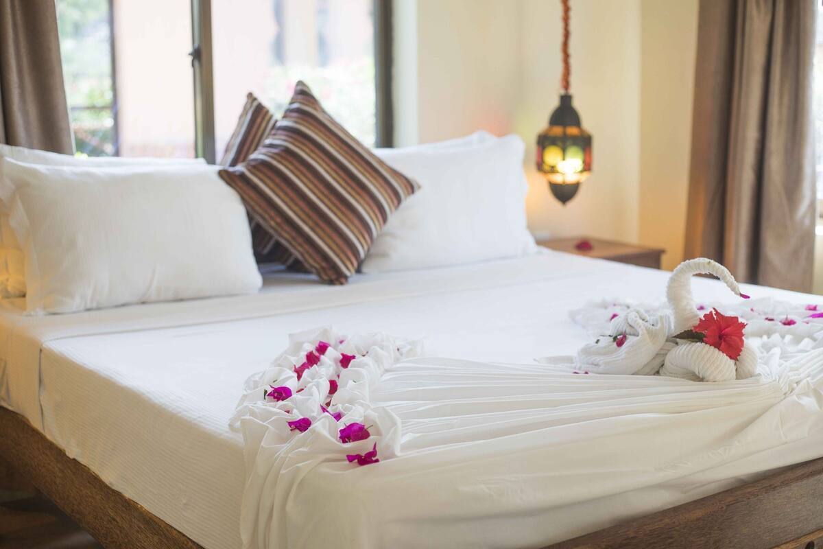 Una cama bien hecha con sábanas blancas, un cojín decorativo con forma de cisne y un farol colgante.
